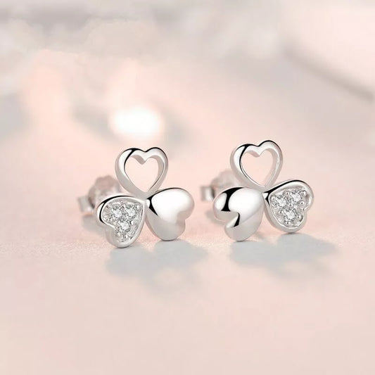 Silver heart-shaped earrings with clear gemstones on a soft pink background